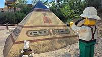 Ein Hase sitzt neben einem Pyramidenforscher aus Legosteinen vor einer Pyramide.