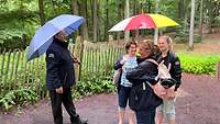 Ein Mann und drei Frauen unterhalten sich unter aufgespannten Regenschirmen.