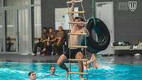 Menschen sind im Schwimmbecken und einer klettert eine Strickleiter hinab in das Becken