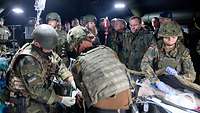 Mehrere Soldaten sthen in einem Zelt. Drei Soldaten behandeln einen Verwundeten.