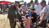 Ein Soldat verteilt Eis an Kinder, die Eltern stehen dabei. 