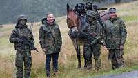 Drei Soldaten und ein Zivilist in Flecktarnparka stehen am Feldrand mit einem Maultier in der Mitte.