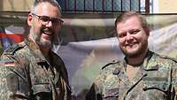 Zwei Soldaten stehen lächelnd vor einem Gebäude.