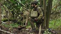 Zwei tschechische Soldaten knien in einem Waldstück. Sie sind nur schwer zu erkennen. 