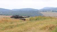 Ein Leopard 2A6 steht hinter einer Erdkuppe. Im Hintergrund kann man eine weite Ebene sehen. 