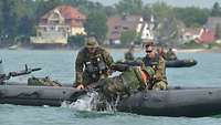 Zwei Soldaten sitzen in einem Schlauchboot und hieven einen dritten aus dem Wasser.