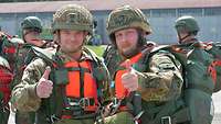 Zwei Soldaten mit orangefarbenen Schwimmwesten stehen nebeneinander und recken die Daumen hoch