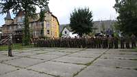 Ein Soldat steht vor einer Formation von Soldatinnen und Soldaten. Einige von ihnen halten ihre Dienststellenwimpel in der Hand.