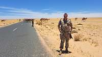 Ein Soldat steht inmitten einer Wüstenlandschaft, neben ihm ist eine Straße.
