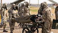 Mehrere Soldaten in Schutzkleidung transportieren eine Trage mit einem Patientensimulator darauf