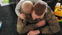 Ein Soldat und sein Sohn liegen auf dem Teppich. Umgeben sind sie von Spielzeug.