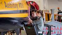 Eine junge Frau und ein junger Mann arbeiten gemeinsam an einem Flugzeug.