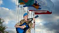Ein Mann mit einer Gitarre steht vor verschiedenen Flaggen.