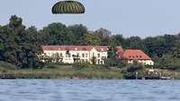 Ein Fallschirmspringer kurz vor der Landung im Wasser. Im Hintergrund ist ein Haus zusehen.