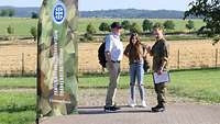 Ein Soldat steht mit einem Mann und einem Mädchen neben einer Beach Flag neben einem Feld. 