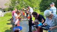 Eine Gruppe von Erwachsenen und Kindern stehen mit Goldwaschpfannen vor einem Wassertrog.