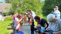 Eine Gruppe von Erwachsenen und Kindern stehen mit Goldwaschpfannen vor einem Wassertrog