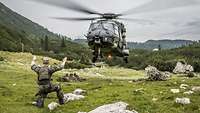 Ein Soldat gibt einen knapp über dem Boden schwebenden Hubschrauber NH-90 Handzeichen