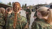 Vor einer Gruppe von jungen Frauen in Uniform stehen zwei Soldaten und erklären etwas.