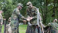 Zwei Soldaten mit Tarnfarbe im Gesicht bauen ein Zelt auf