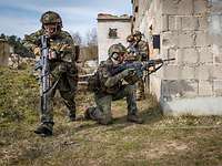 Drei bewaffnete Soldaten stehen und hocken nahe einer Hausmauer und sichern nach allen Seiten.