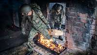 Zwei Soldaten tragen eine Munitionskiste durch eine Tür über ein Feuerhindernis.