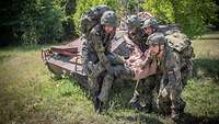 Vier Soldaten tragen einen verwundeten Kameraden aus dem Gelände zu einem Sammelpunkt.