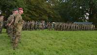 Reservistendienstleistende im Feldanzug stehen in K-Form in Linie angetreten auf einer Wiese.