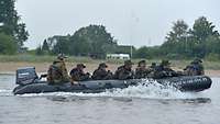 Ein Schlauchboot mit Außenbordmotor, besetzt mit sieben Soldaten, fährt auf einem Fluss.
