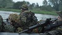 Soldaten sitzen in einem Schlauchboot, mit ihren Gewehren sichern sich nach außen.