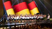 Das deutsche Team steht auf der Tribüne. Im Hintergrund ist die Deutschlandfahne zu sehen.