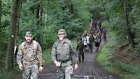 Soldaten und zivile Teilnehmende marschieren durch einen Wald 