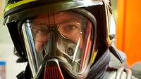 Ein Feuerwehrmann mit einem gelben Helm und einer Atemschutzmaske blickt den Betrachter direkt an.