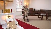 Eine Militärpfarrerin in Uniform sitzt auf einer Bank in einer Kapelle.