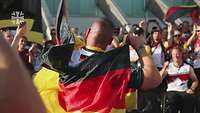 Ein deutscher Athlet jubelt mit Deutschlandflagge und wird von Fans beklatscht.