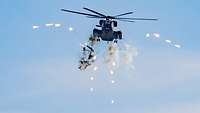 Ein fliegender Hubschrauber ist umringt von leuchtenden Teilchen. Unter dem Hubschrauber ist Rauch.
