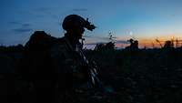 Silhouette eines Soldaten mit Helm, Nachsichtgerät und Rucksack auf dem Rücken in der Abenddämmerung