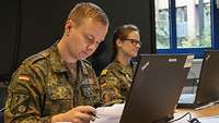Ein Soldat und eine Soldatin, die jeweils an einem Laptop arbeiten. 