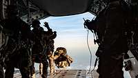 Soldaten stehen an der geöffneten Heckrampe eins Flugzeugs, einer springt raus.