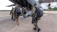 Soldaten mit gepackten Fallschirmen auf dem Rücken laufen über die Heckrampe in ein Flugzeug.