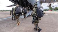 Soldaten mit angelegter Ausrüstung, Waffen und Fallschirm betreten ein Transportflugzeug.