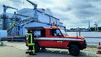 Ein Feuerwehrmann bereitet an einem Feuerwehrfahrzeug ein Lagebild vor, im Hintergrund ein Dock