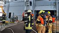Mehrere Feuerwehrleute auf dem Helideck eines Kriegsschiffes