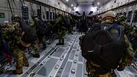 Zahlreiche Soldaten legen ihr Sprunggepäck in einem Flugzeug an.