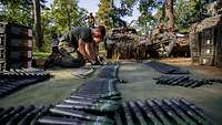 Soldaten hocken am Boden und bereiten Munitionsgurte vor. Munition liegt gut sortiert um sie herum.