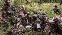 Viele Soldaten sitzen in einer Gruppe in hohem Grass im Wald.