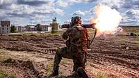 Ein Soldat feuert mit der Panzerfaust Richtung Häuser. Ein Feuerball entsteht.
