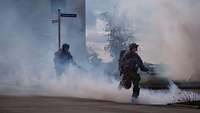 Im Nebel überqueren mehrere Soldaten mit Gewehr eine Straße rennend.