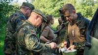 Zwei Soldaten schenken aus Wärmebehältern Essen an Soldaten mit Kochgeschirr aus.