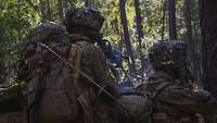 Zwei Soldaten liegen im Wald in Stellung und feuern mit dem Maschinengewehr.